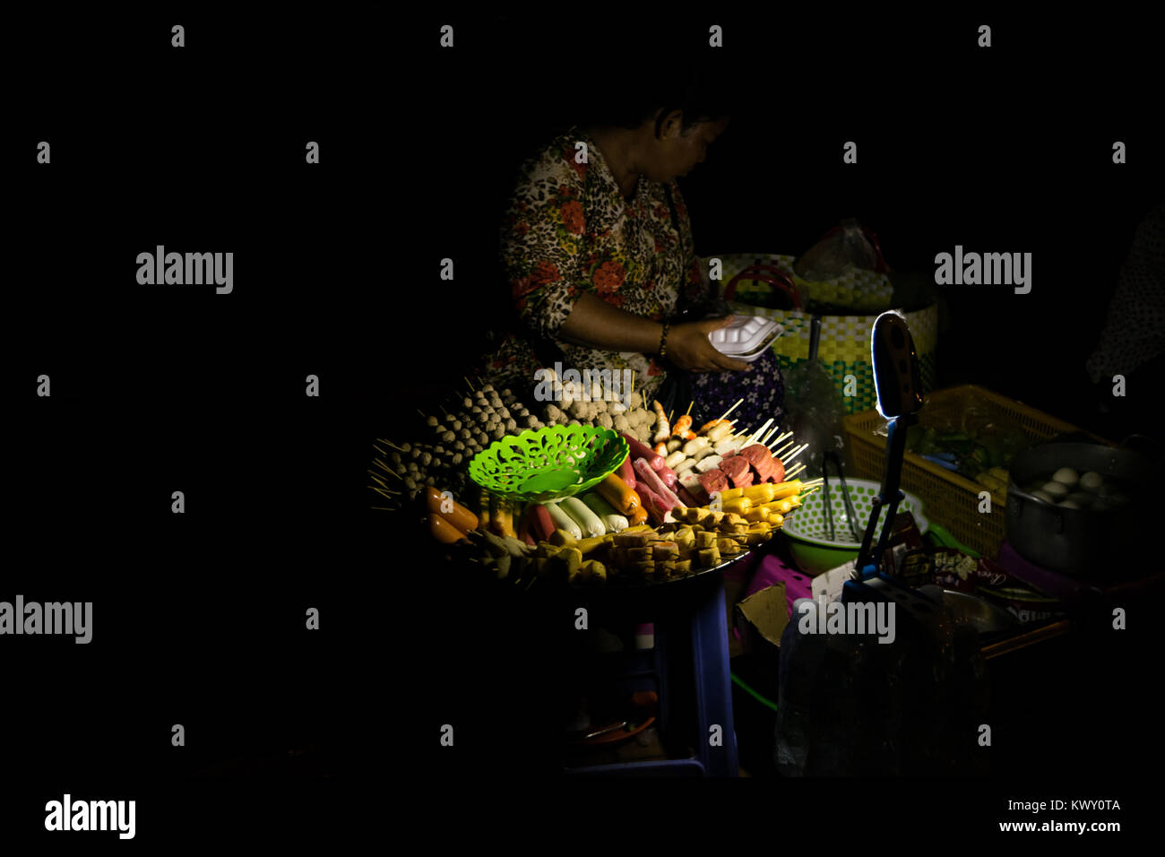 Una donna asiatica la vendita di cibo di strada di notte: alimenti trasformati, salsicce e spiedini, visualizzato nel piatto rotondo. Phnom Penh, Cambogia, sud-est asiatico Foto Stock