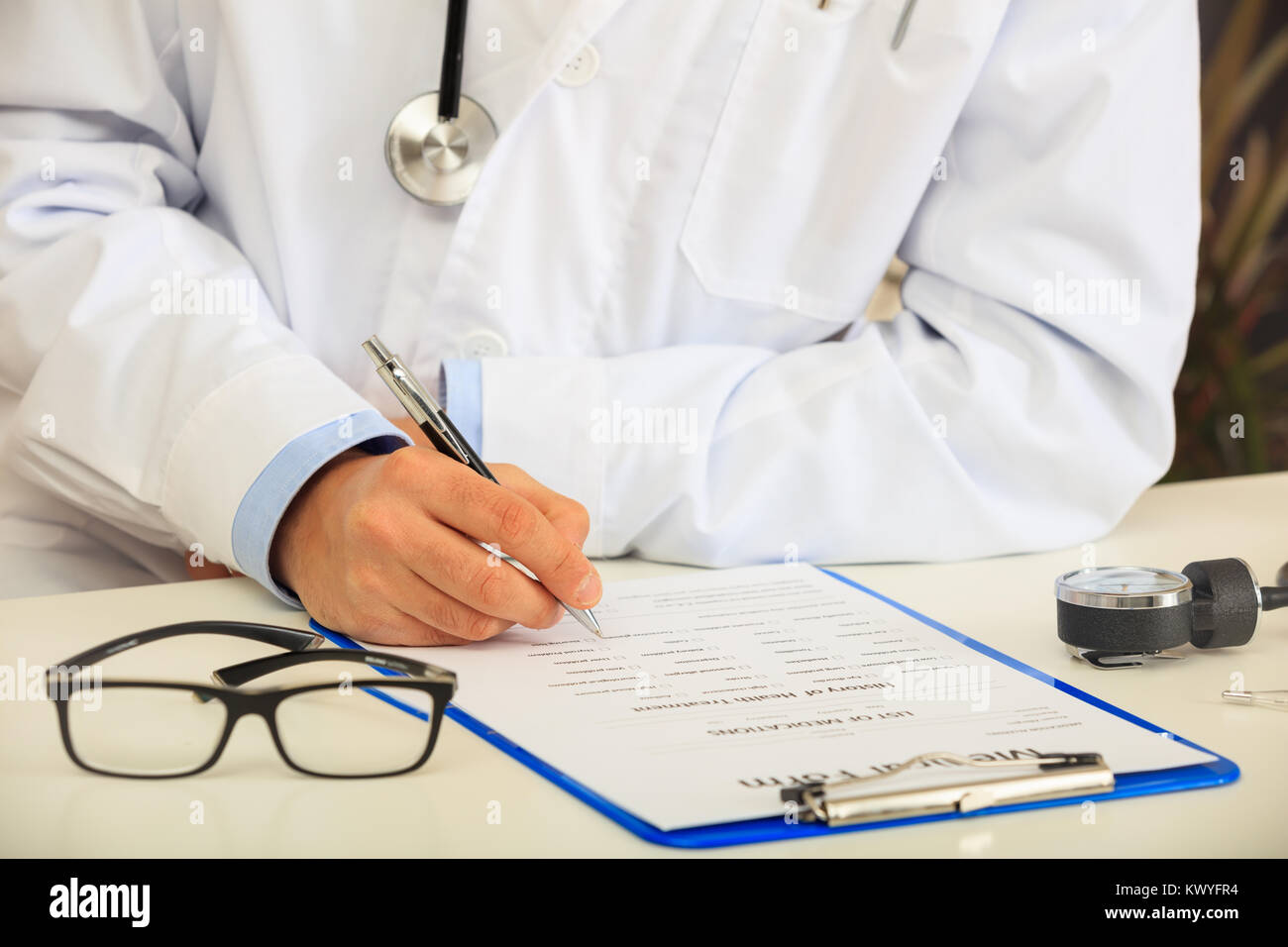 Medico di riempimento di una forma medica sulla sua scrivania Foto Stock