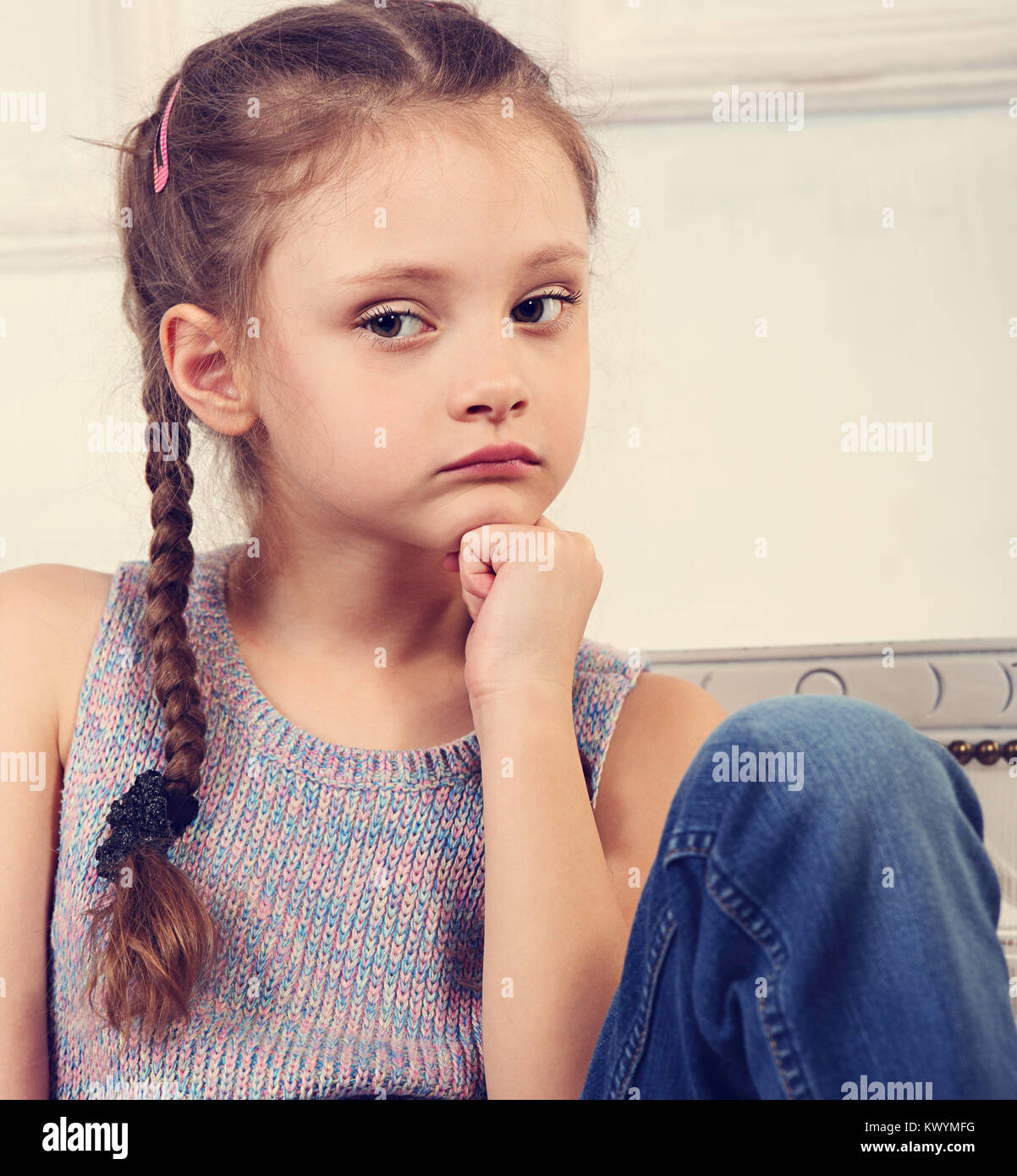 Bellissimo il pensiero serio carino kid ragazza seduta sul banco in blue jeans e guardando triste. Closeup ritratto Foto Stock