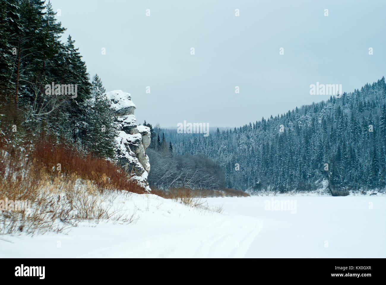 Uno scoglio pittoresco sulla riva di un inverno Congelato stagno nelle montagne boscose Foto Stock
