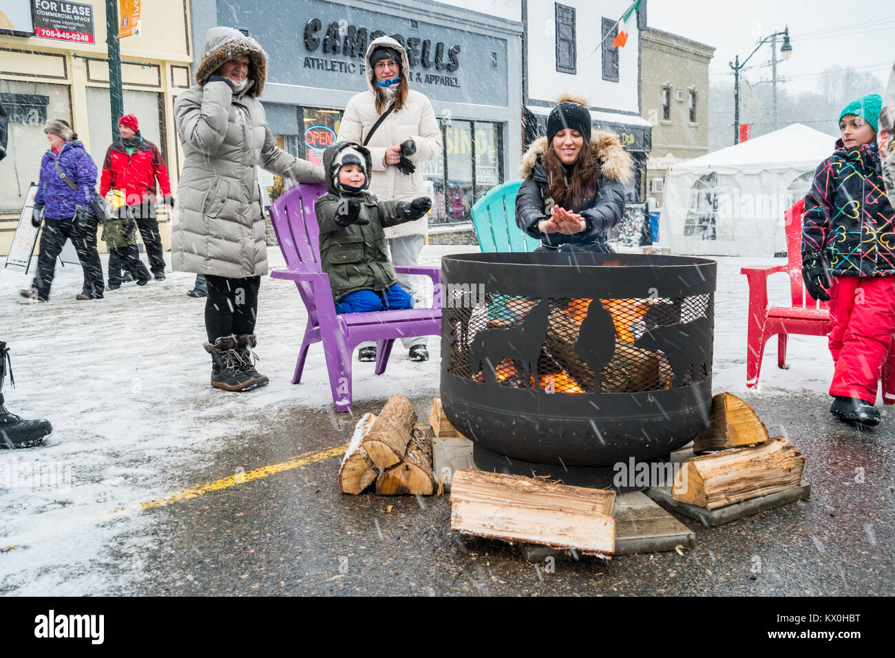 Le persone calde fino a una buca per il fuoco durante il fuoco e il ghiaccio Festival in downtown Bracebridge, Ontario, Canada. Foto Stock
