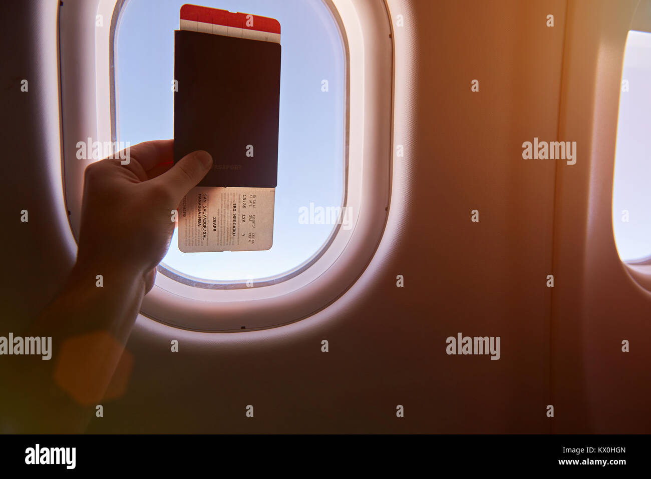 Tenere in mano il passaporto in aereo sulla finestra con cielo azzurro sfondo Foto Stock