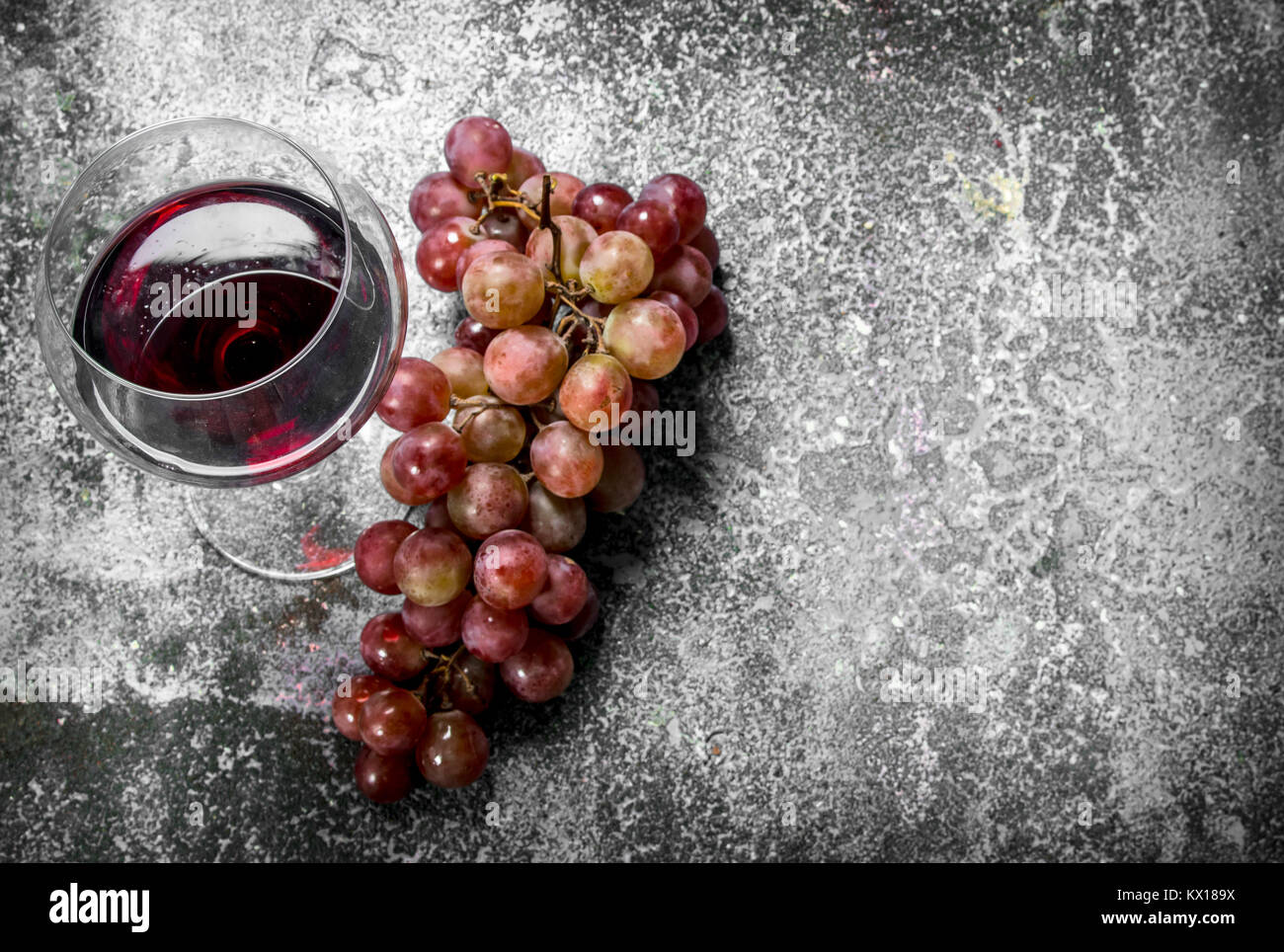 Bicchiere di vino rosso con un ramo di uve fresche. Su uno sfondo rustico. Foto Stock