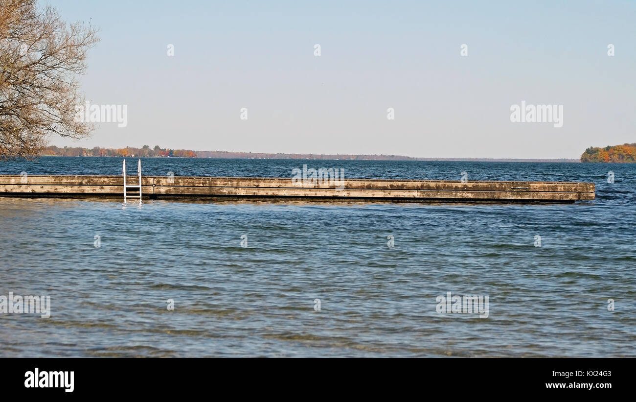 Un lungo legno piscina vuota dock raggiungendo fuori in un bellissimo lago blu. Alberi di colore di autunno può essere visto nel lontano sullo sfondo. Foto Stock