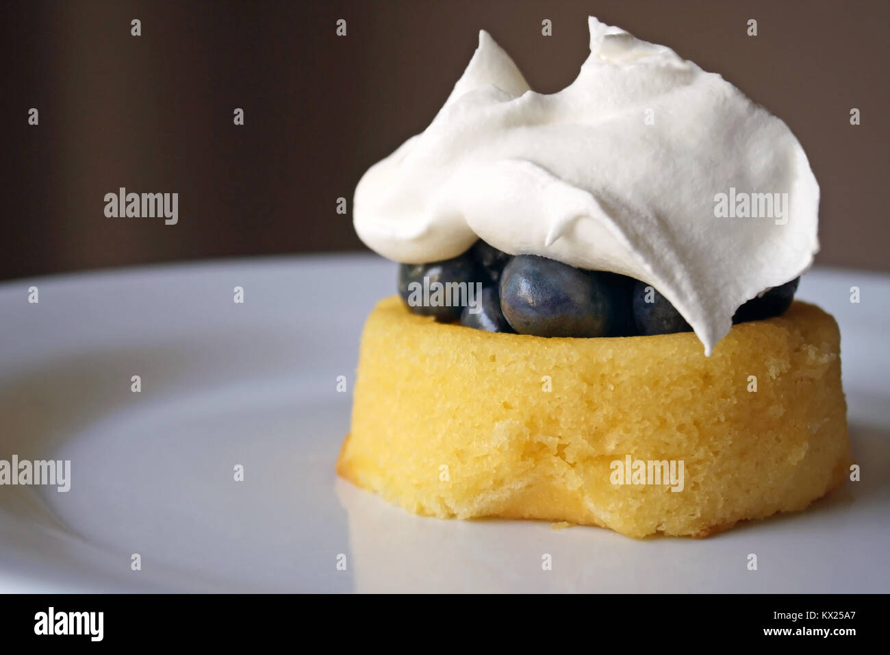 Fresche dolci mirtilli su un mini pan di spagna condito con morbidi di panna montata Foto Stock