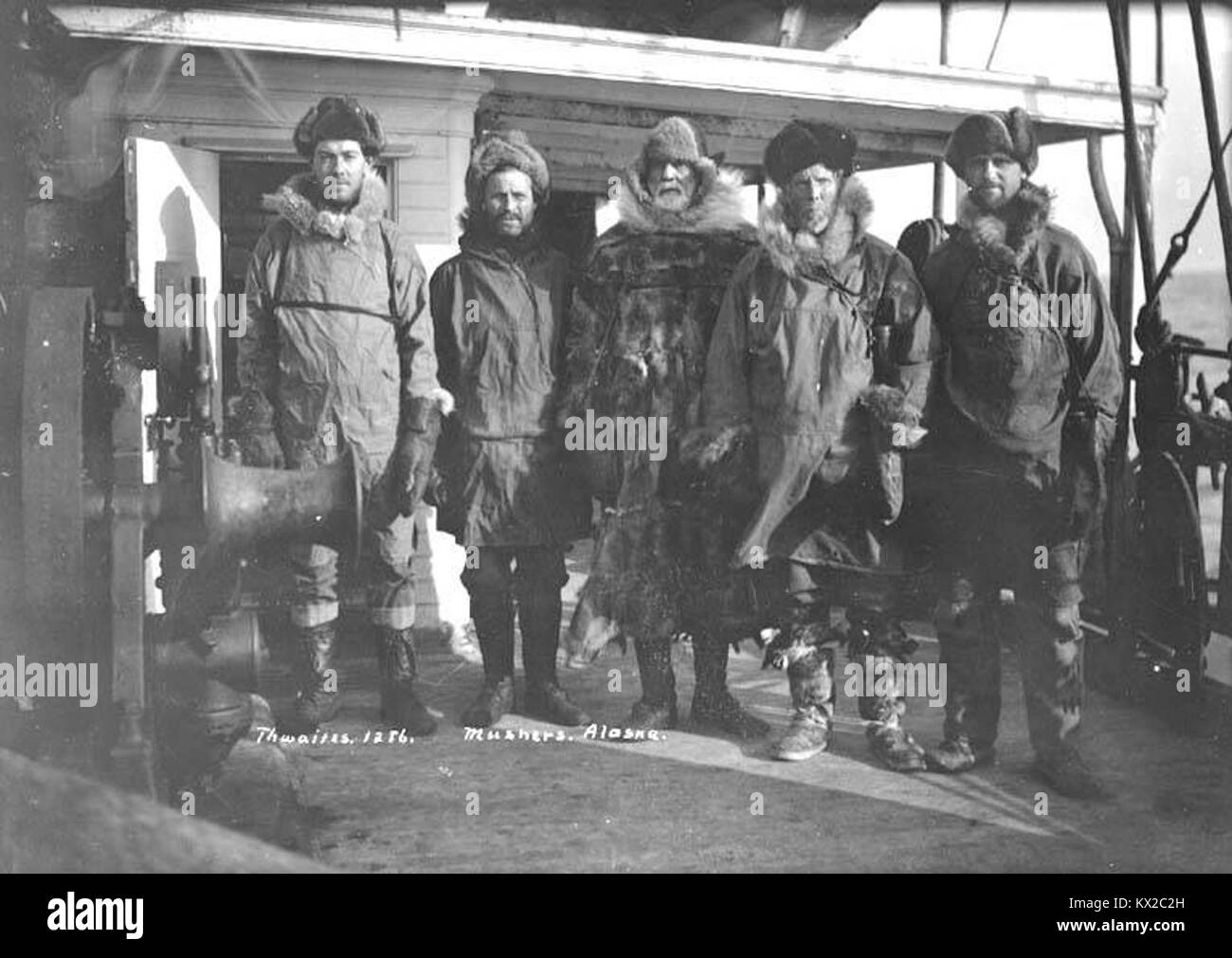 Questa fotografia del 1910 circa mostra cinque uomini equipaggiati con outerwear artico in piedi con una squadra di slitte trainate da cani, identificati come "musher". L'immagine riflette le pratiche di slitte trainate da cani all'inizio del XX secolo e l'abbigliamento da spedizione in climi freddi. Wikimedia Commons Foto Stock