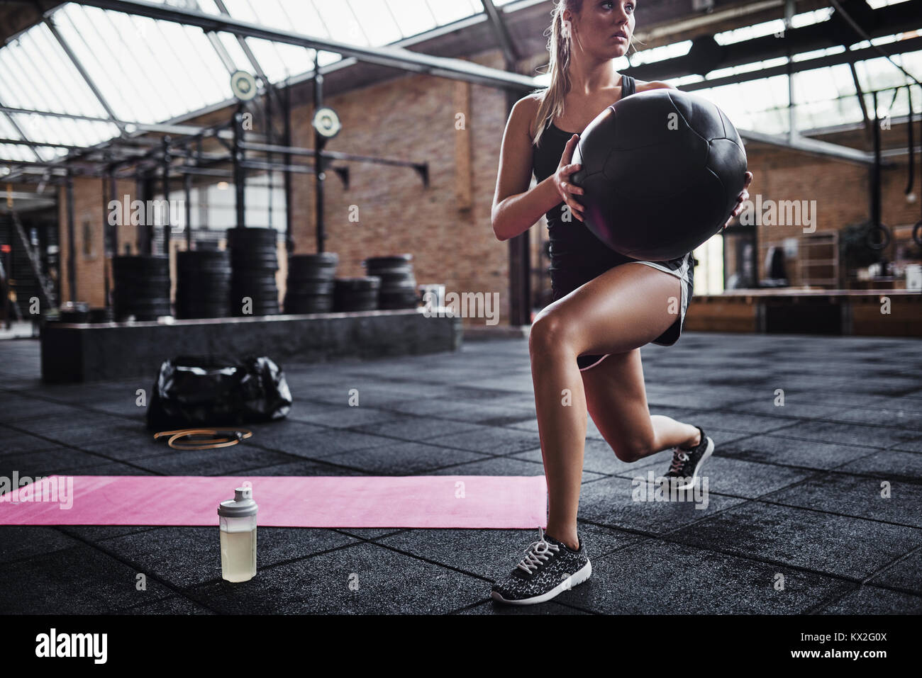 Montare la giovane donna in abbigliamento sportivo facendo esercizi di nucleo con una palla ginnica mentre si lavora fuori da solo in una palestra Foto Stock