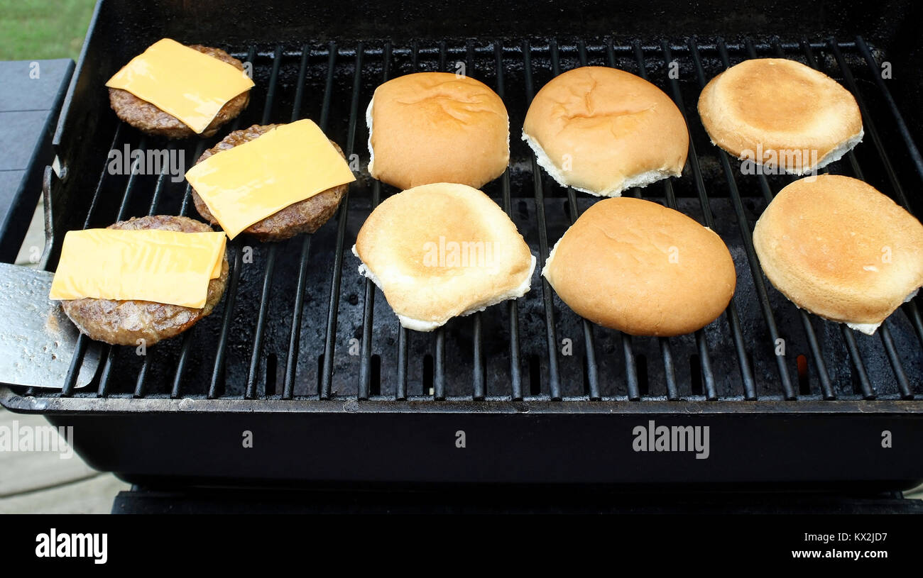 Patties di hamburger con il formaggio lavorato fette di cottura su un tavolo esterno top barbecue. Panini al fianco di tostatura Foto Stock