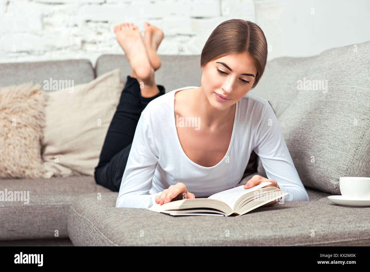 Giovane bella donna sdraiata sul divano a leggere un libro nel salotto di  casa Foto stock - Alamy