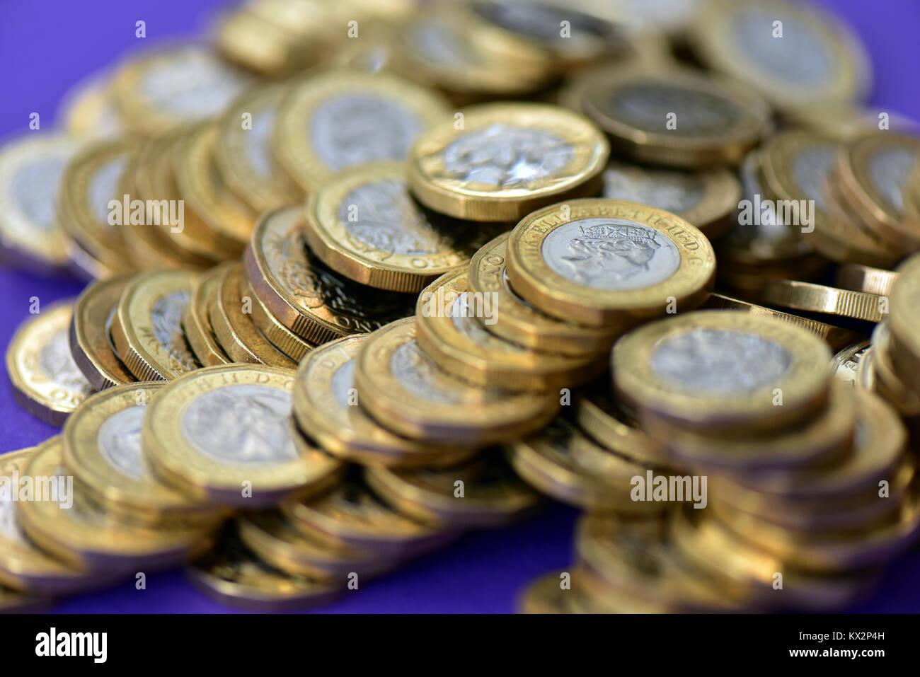 Un gran mucchio di una libbra di monete in un colorato viola malva o sfondo. Pile di denaro o di contanti e monete d oro e d argento usato in GB valuta. Foto Stock