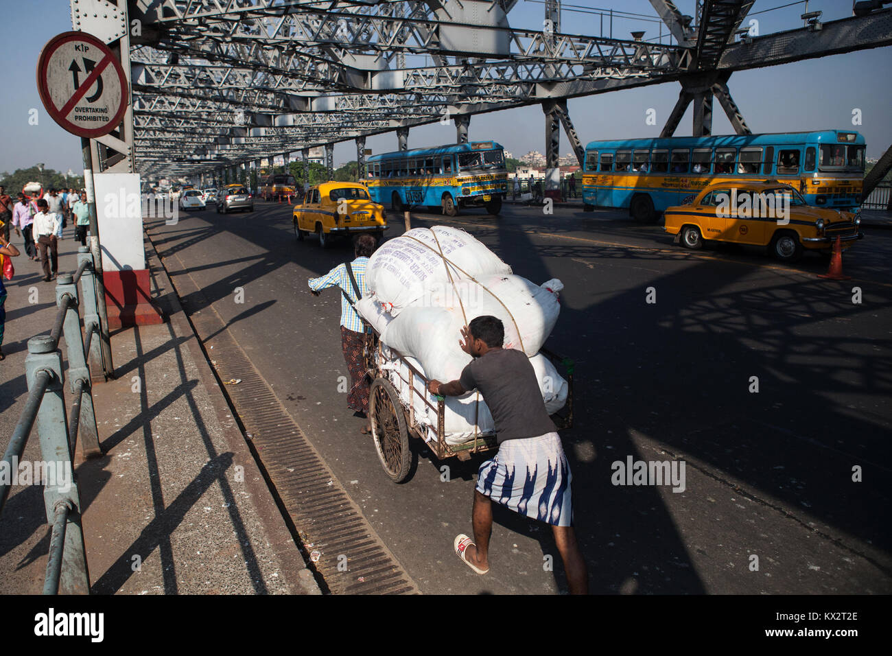 Gli uomini spingere un carrello overladen attraverso il ponte di quella di Howrah in Kolkata, India Foto Stock