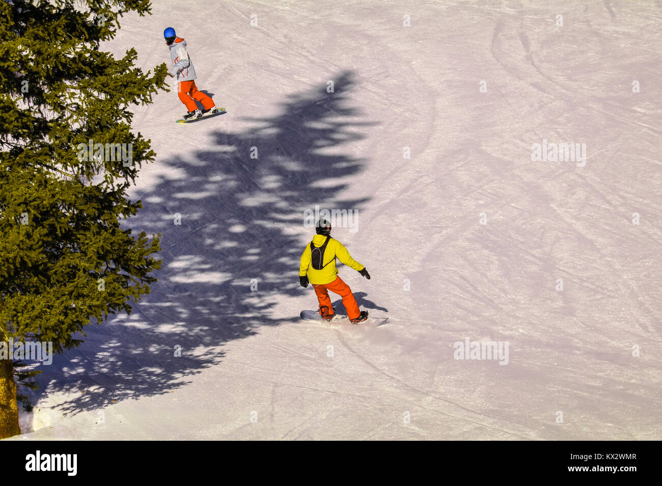 Giovani snowboarder scendendo lungo un pendio nevoso, suo istruttore davanti a lui; vista da sopra Foto Stock