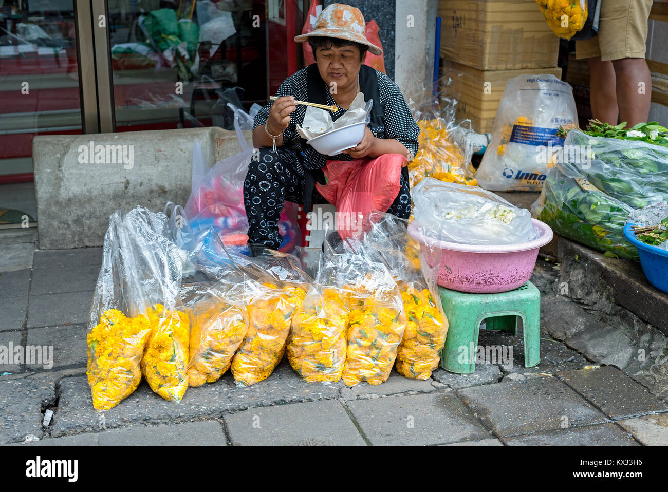 Un thai venditore ambulante prende la sua pausa pranzo da vendere grandi borse di garofani giallo su un lato di Bangkok street. Foto Stock