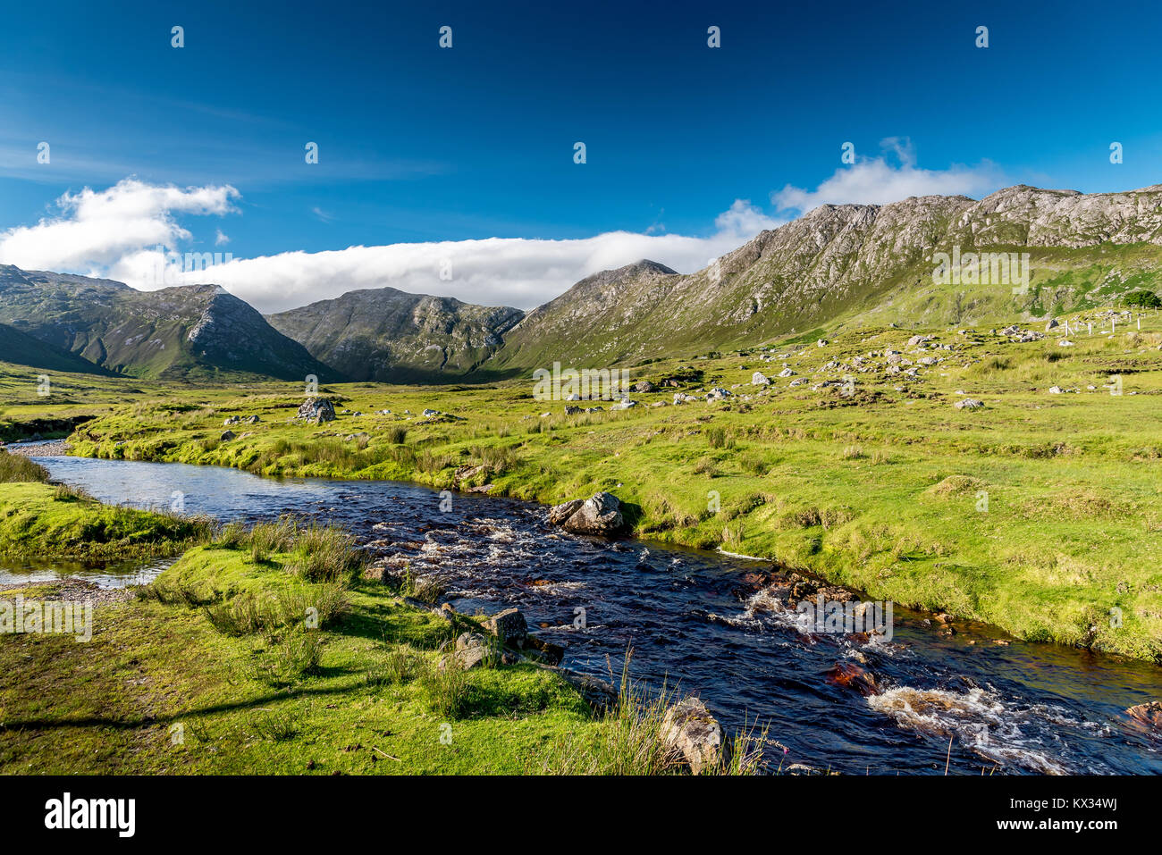 Paesaggio di Connemara in Irlanda: Un fiume scorre in mezzo ai prati di fronte al maestoso Twelve Bens montagne Foto Stock