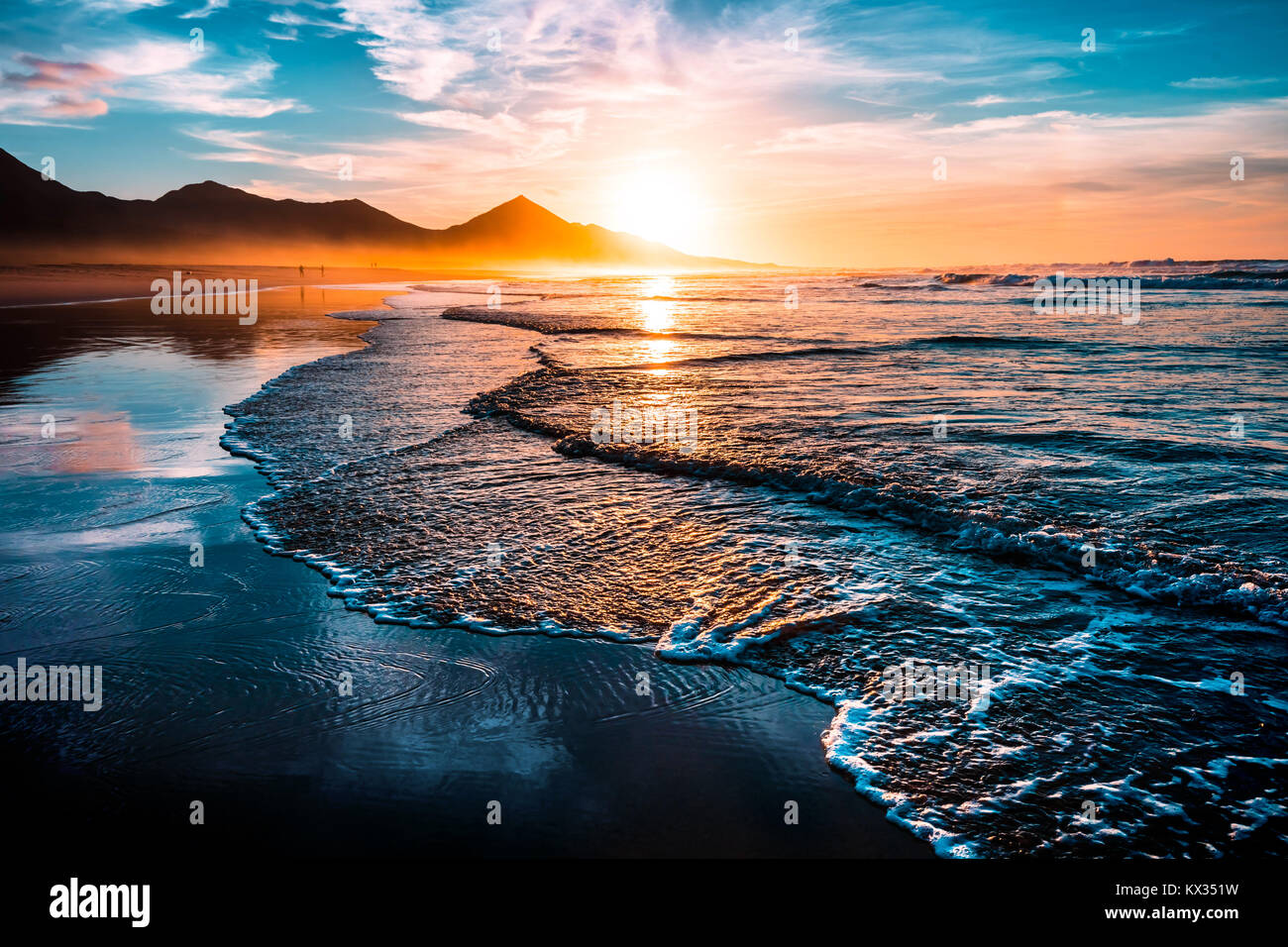 Straordinaria spiaggia tramonto con orizzonte infinito e Solitarie figure nella distanza e incredibile onde schiumoso. Colline vulcaniche in background. Foto Stock