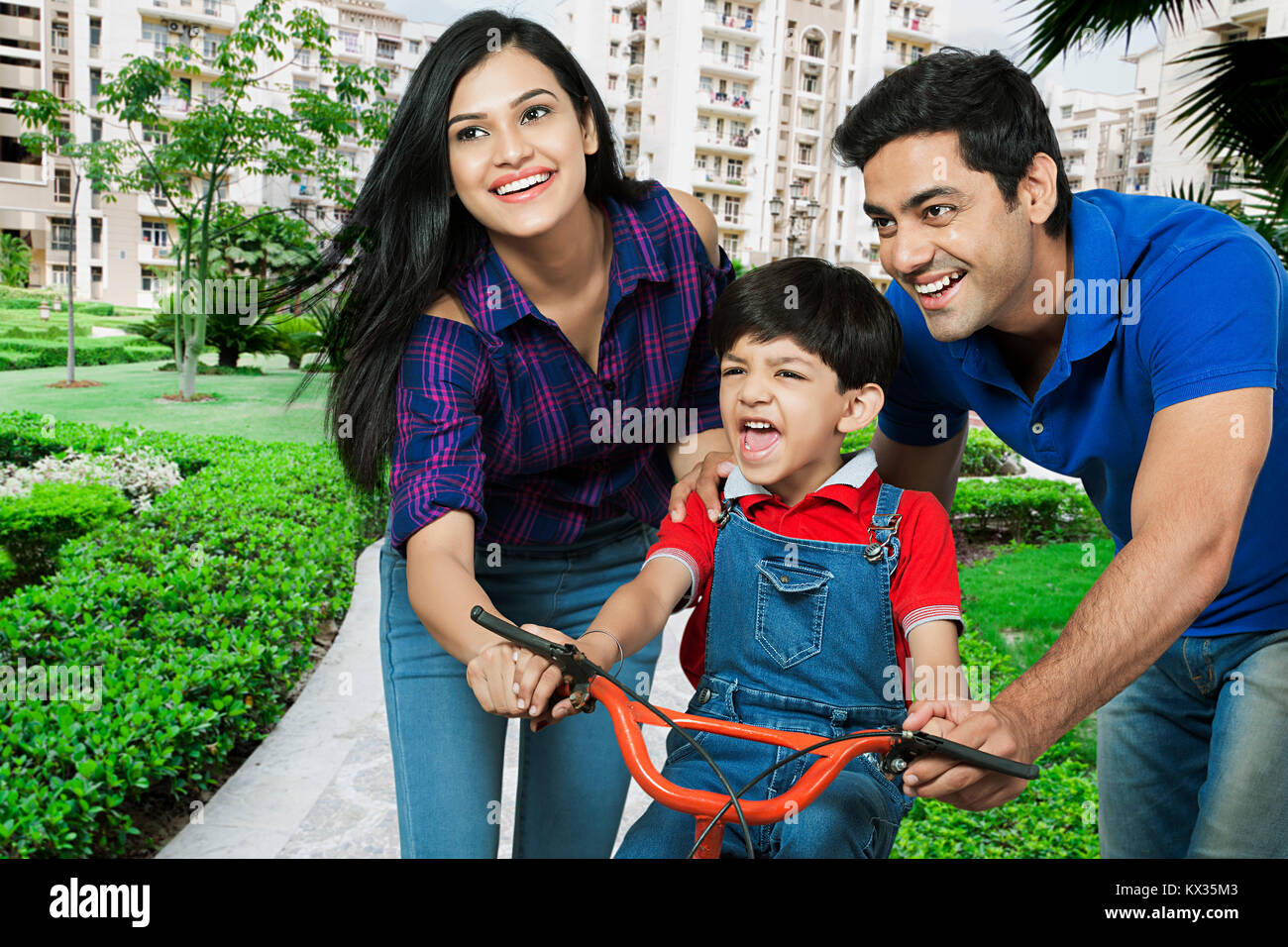 La famiglia felice- genitori aiutando figlio al ciclo di marcia In-Park Foto Stock