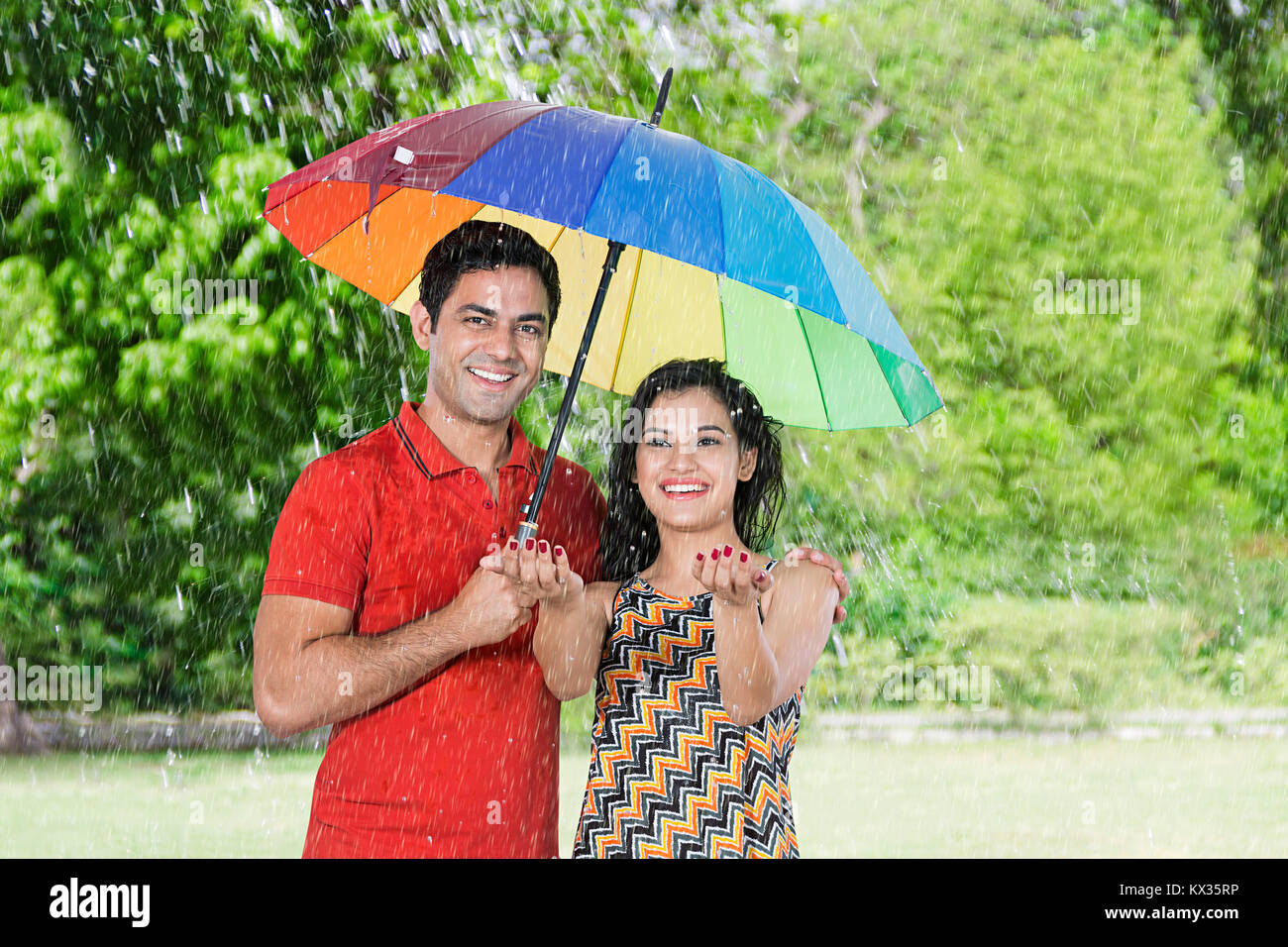 Felice l'uomo e la donna giovane sotto ombrellone in estate il parco-pioggia Foto Stock