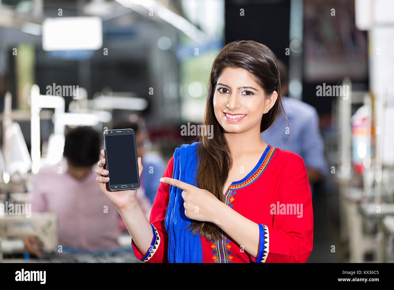 1 lavoratore di sesso femminile che sarto che mostra lo smartphone nel laboratorio di cucito Foto Stock