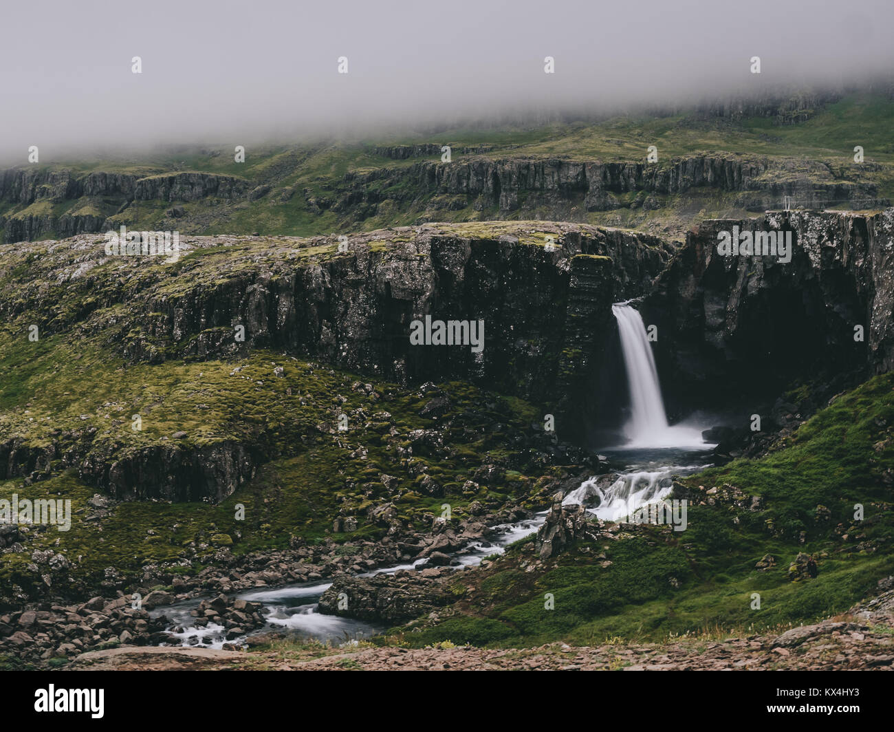 Bellissima vista della scogliera con cascata a nebbioso giorno in Islanda Foto Stock