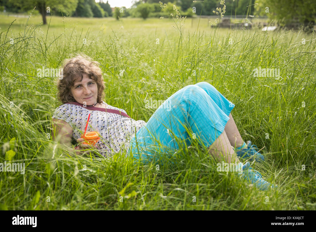 La donna è sdraiato in mezzo all'erba alta con un bicchiere di Aperol Spritz Foto Stock