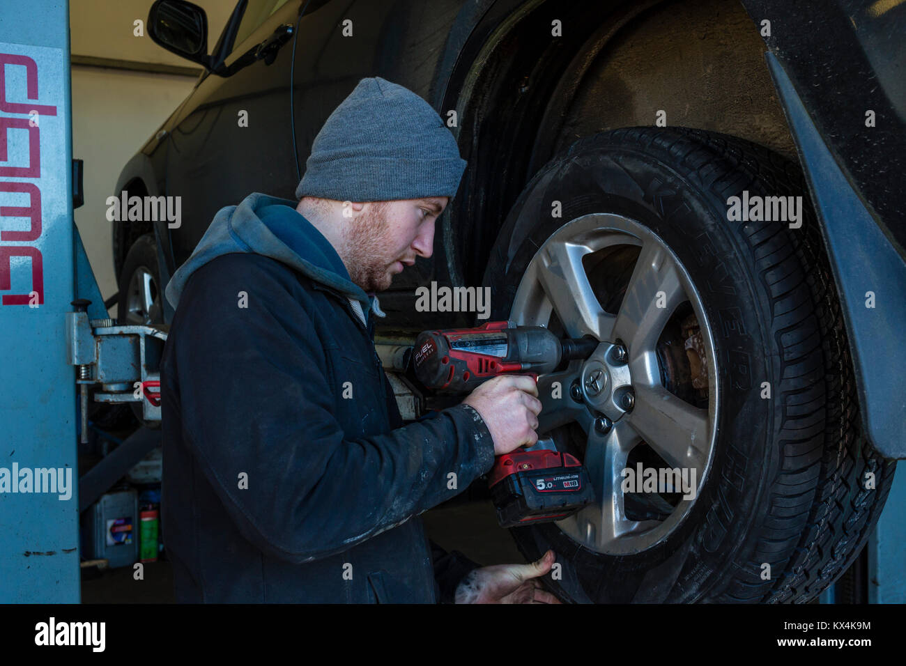 Giovane apprendista meccanico la rimozione di una ruota auto con una chiave a percussione senza fili Foto Stock