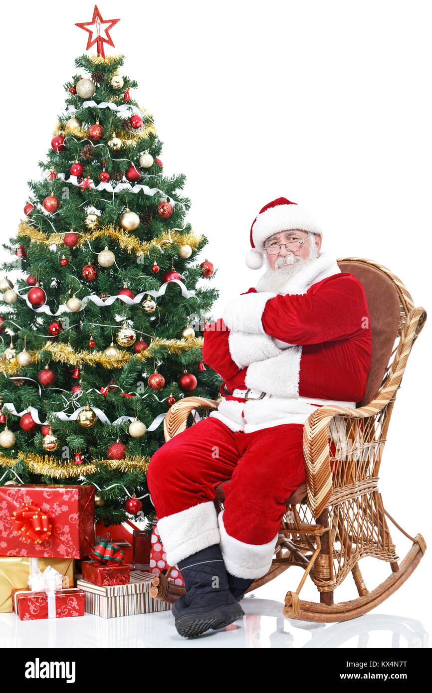 Babbo Natale seduto nella sedia a dondolo accanto pieno albero di Natale decorato, isolato su sfondo bianco Foto Stock