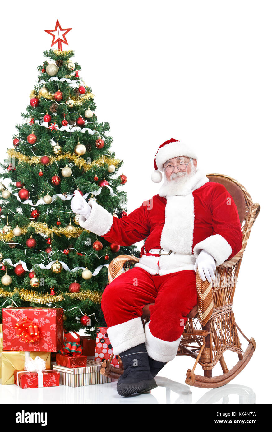 Babbo Natale seduto accanto ad albero di Natale che mostra il pollice fino a firmare, isolati su sfondo bianco Foto Stock