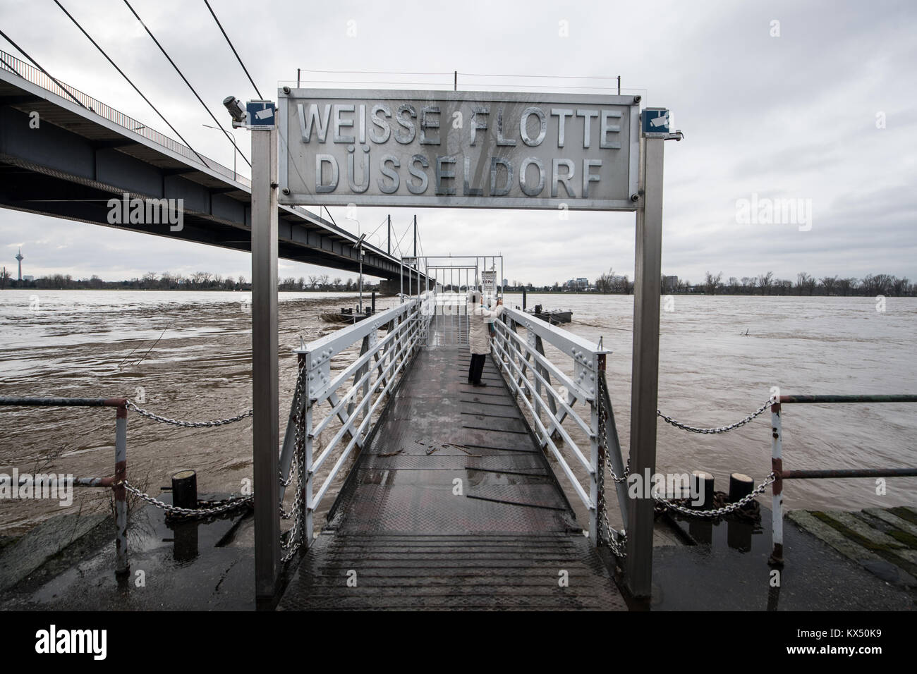 Duesseldorf, Germania. Il 7 gennaio, 2018. Una donna in piedi su un molo del "Weisse Flotte' escursione barche e prende una foto del fiume Reno durante il livello di acqua alta a Duesseldorf in Germania, 7 gennaio 2018. Credito: Bernd Thissen/dpa/Alamy Live News Foto Stock