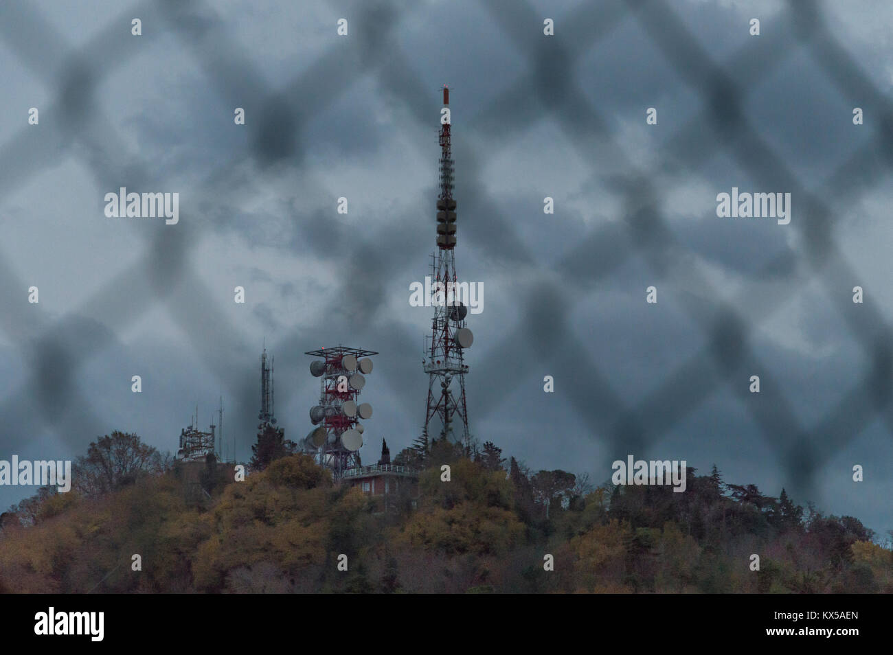 Telecomunicazioni Antenna radio e TV Tower con cielo blu dietro una recinzione di catena Foto Stock