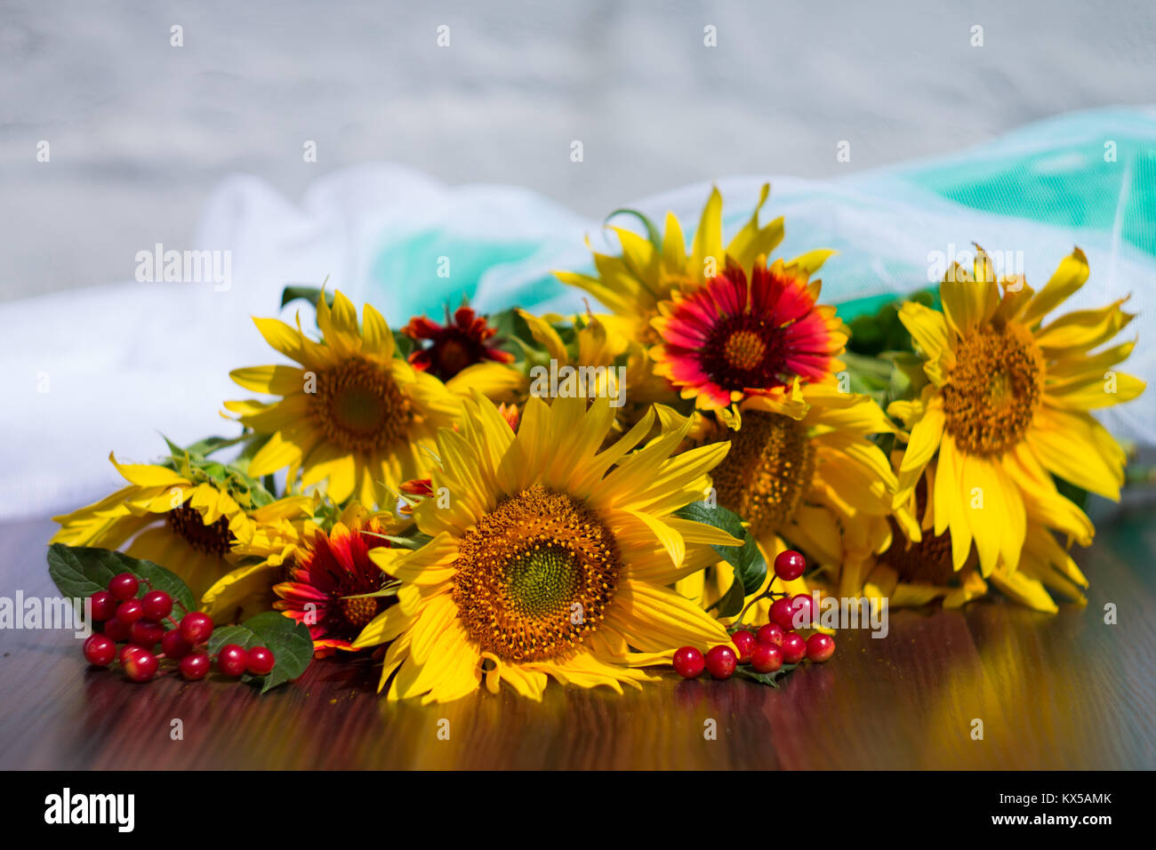 Girasoli, pallon di maggio e fiori di colore rosso su bianco sfocata e panno verde su un tavolo di legno Foto Stock