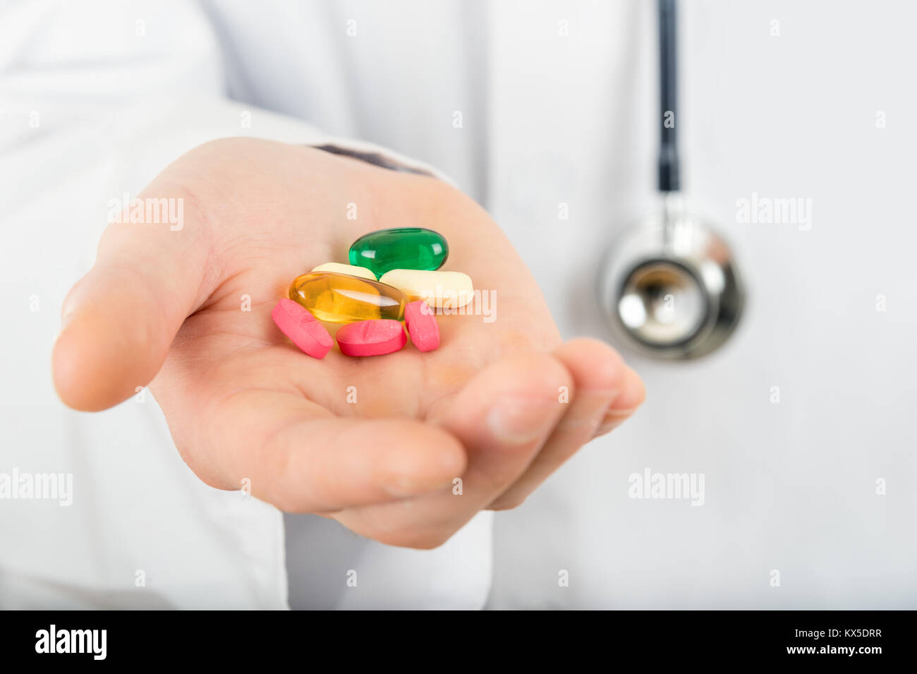 Diversi tipi di pillole di farmaco nella mano di un medico tenendo uno stetoscopio Foto Stock