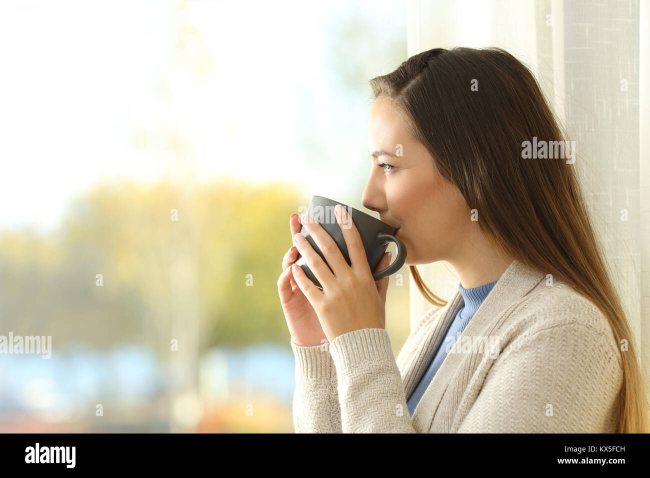 Vista laterale ritratto di una dama rilassato bere il caffè e guardare all'esterno attraverso una finestra a casa Foto Stock