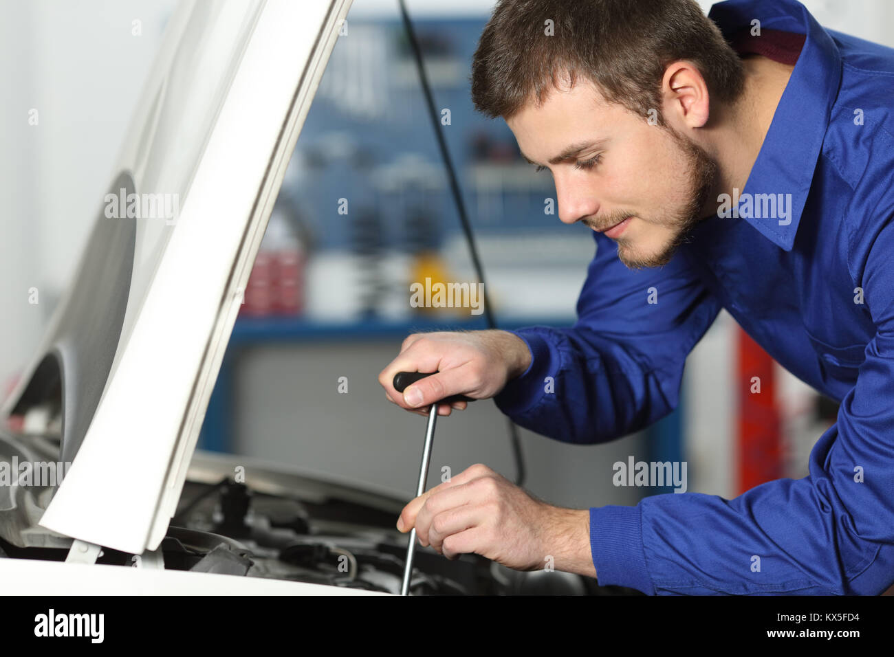 Giovanissimo meccanico la riparazione di un auto in una officina meccanica Foto Stock