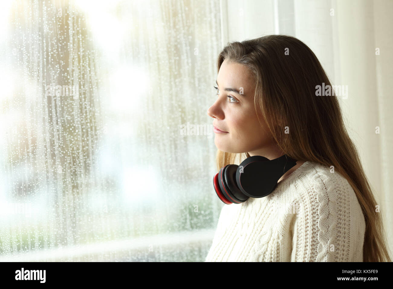 Ritratto di un pensieroso teen di guardare attraverso una finestra in un giorno di pioggia a casa Foto Stock