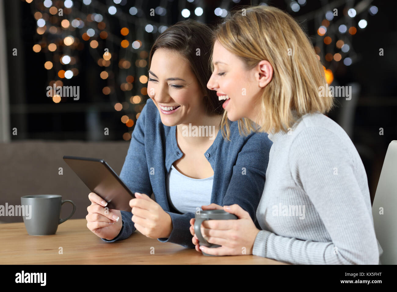 Due felici gli amici a guardare i contenuti multimediali in un tablet seduti a un tavolo a casa di notte Foto Stock