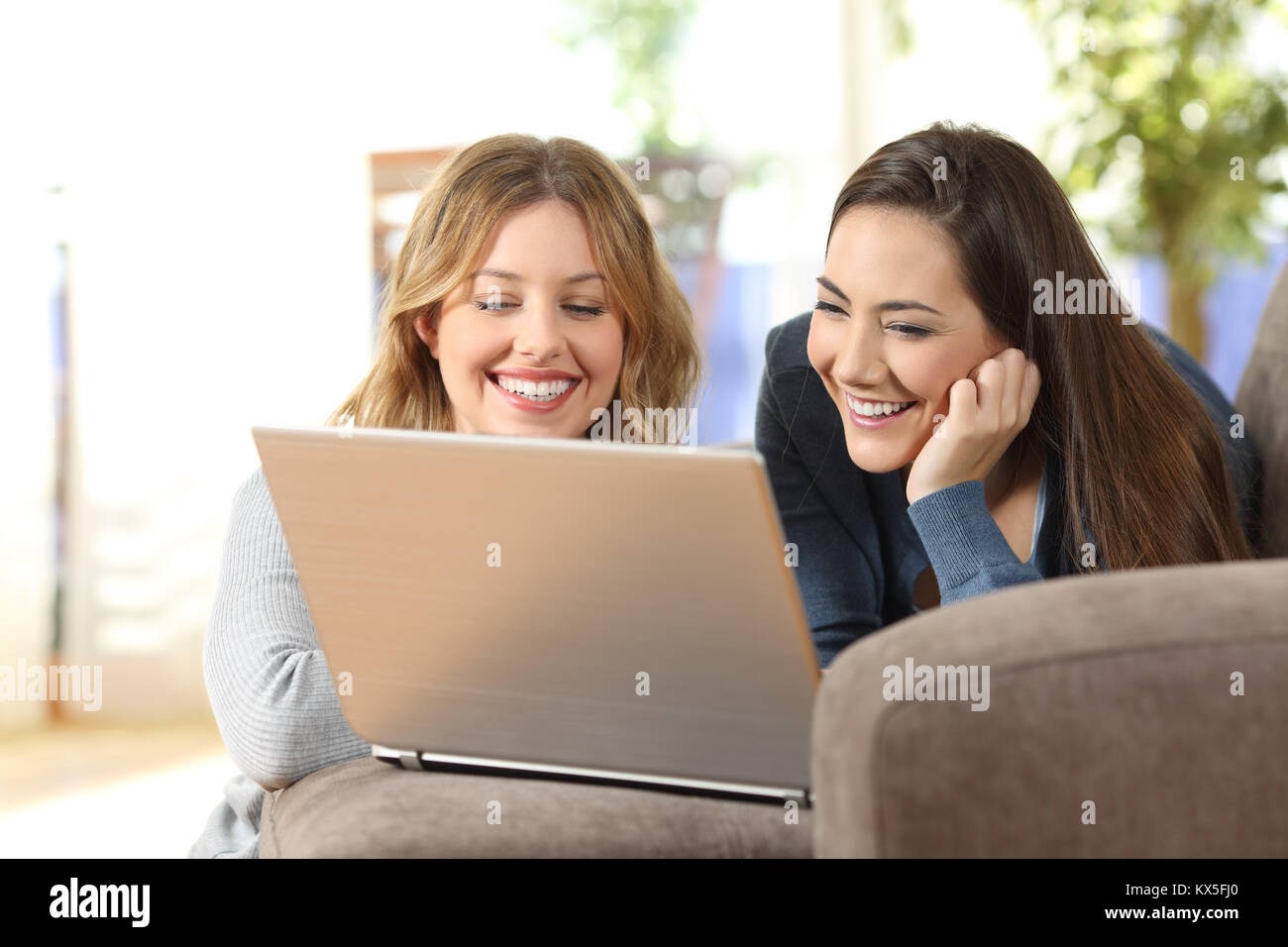 Due lieti compagni di guardare on line il contenuto in un computer portatile che giace su un divano nel salotto di casa Foto Stock