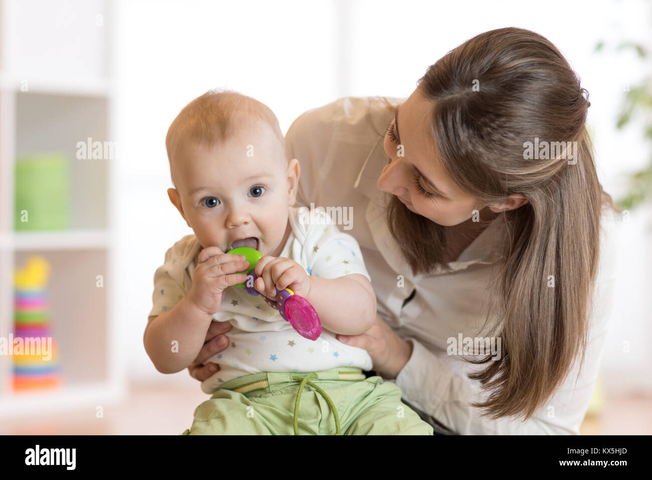 Bambino seduto sulle ginocchia di mom morsi toy Foto Stock