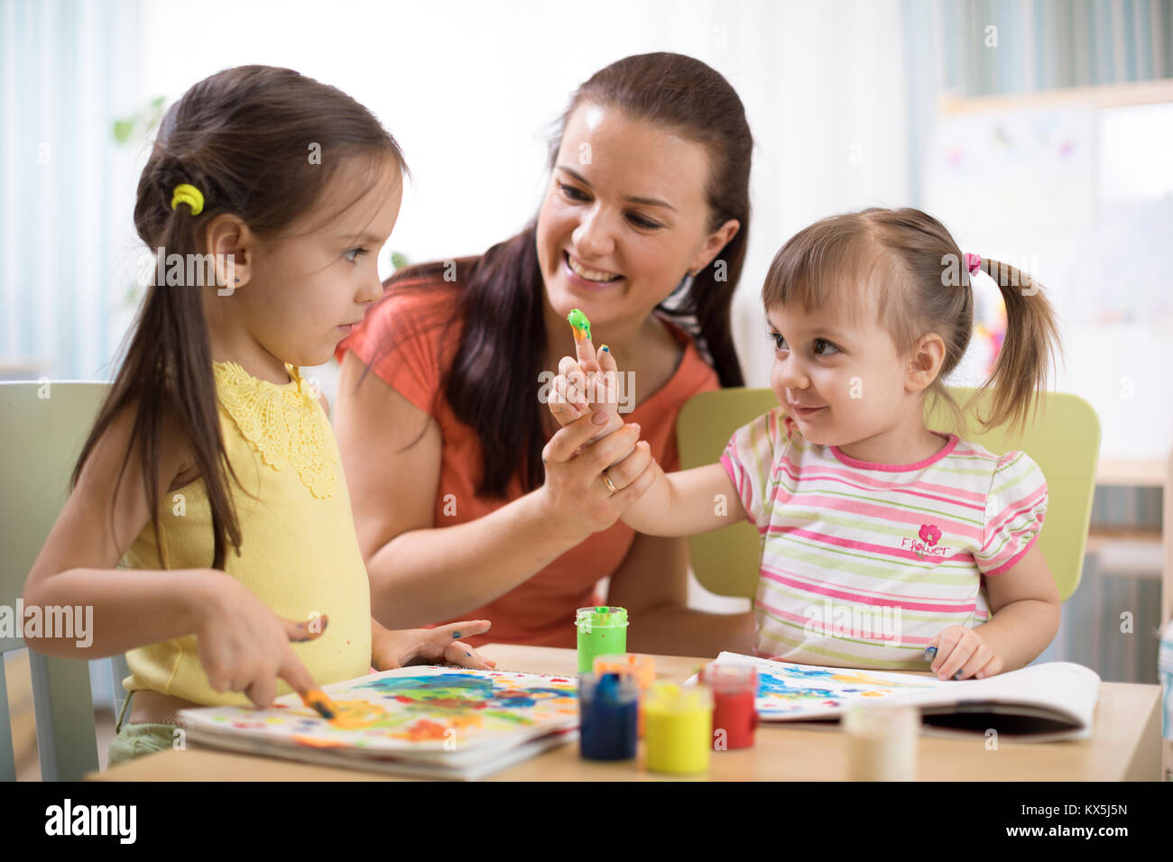 I bambini con la giovane donna insegnante di pittura su tavola insieme a scuola o a casa. Foto Stock