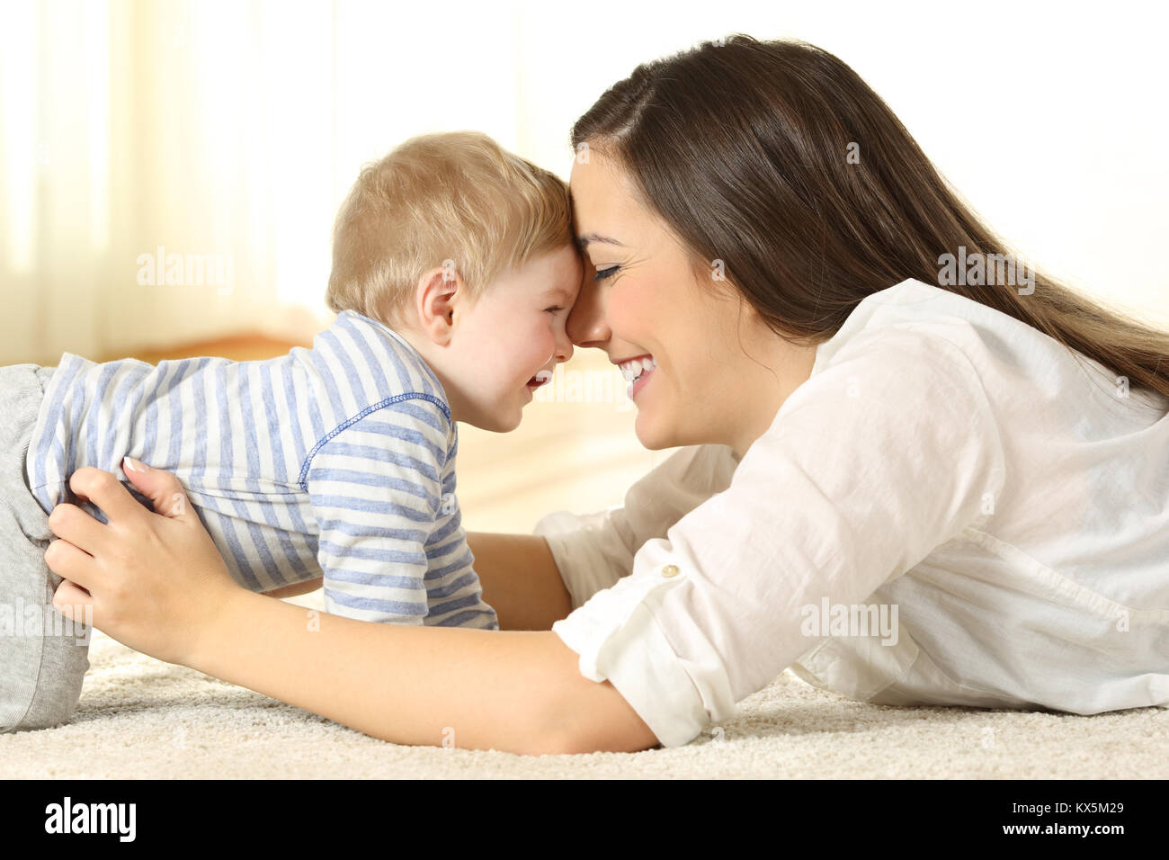 Vista laterale ritratto di una madre affettuosa con scherzando il suo bambino giacente su un tappeto a casa Foto Stock