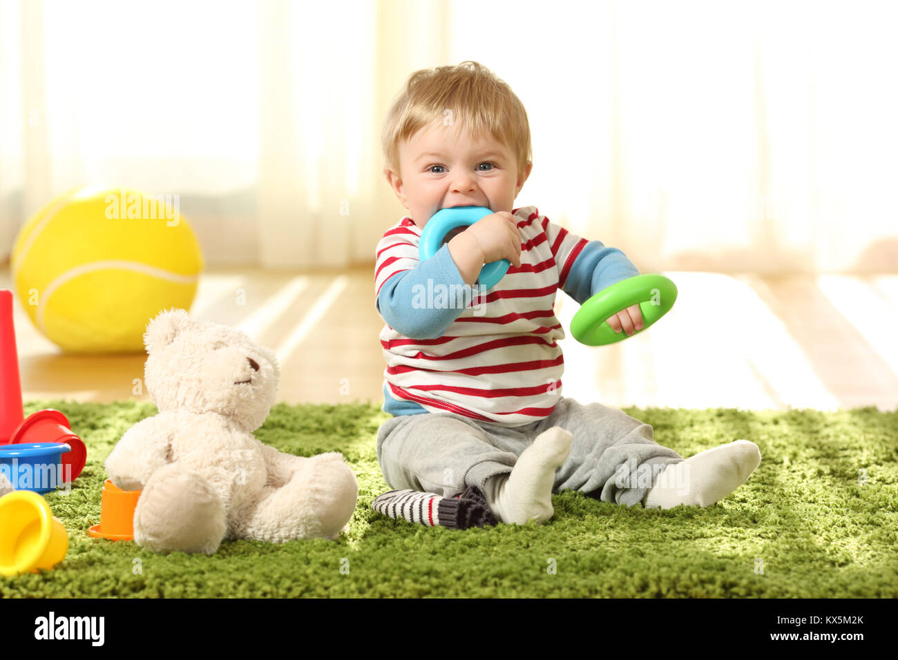 Vista anteriore verticale di un happy baby mordere giocattoli su un tappeto a casa Foto Stock