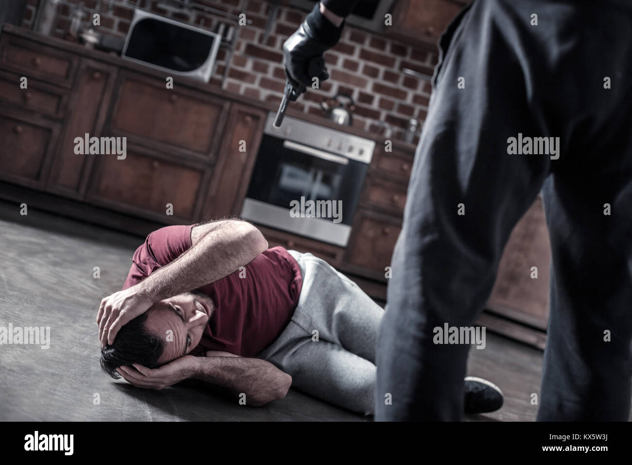 Scioccato uomo disteso sul pavimento e killer con la pistola Foto Stock