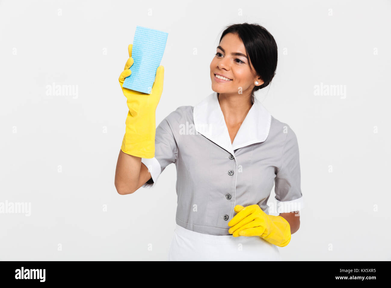 Ritratto di un felice piuttosto governante vestito in uniforme di pulizia  con una spugna rimanendo isolate su sfondo bianco Foto stock - Alamy