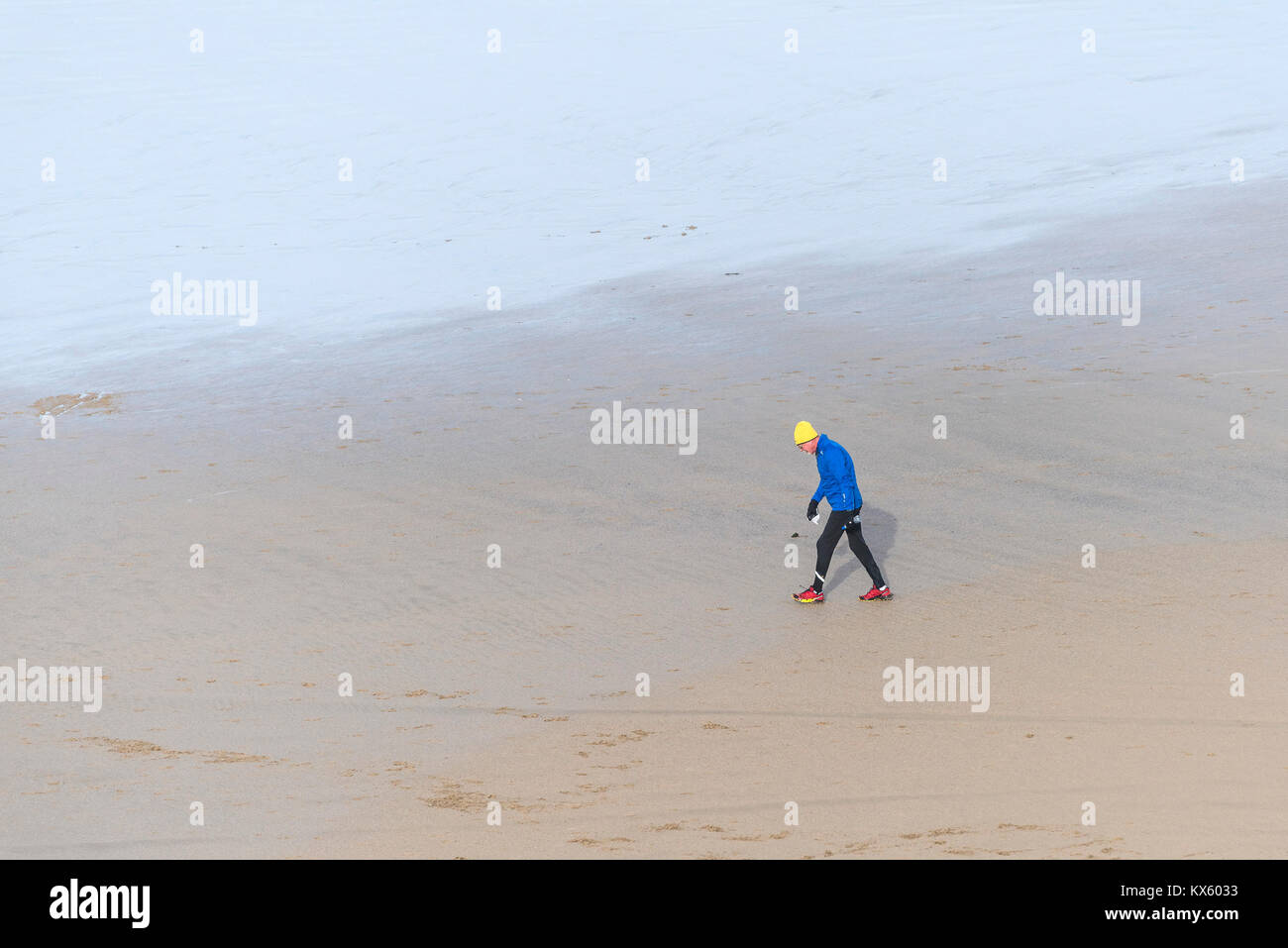 Un uomo maturo che indossa abiti colorati aross a piedi una spiaggia con la bassa marea. Foto Stock