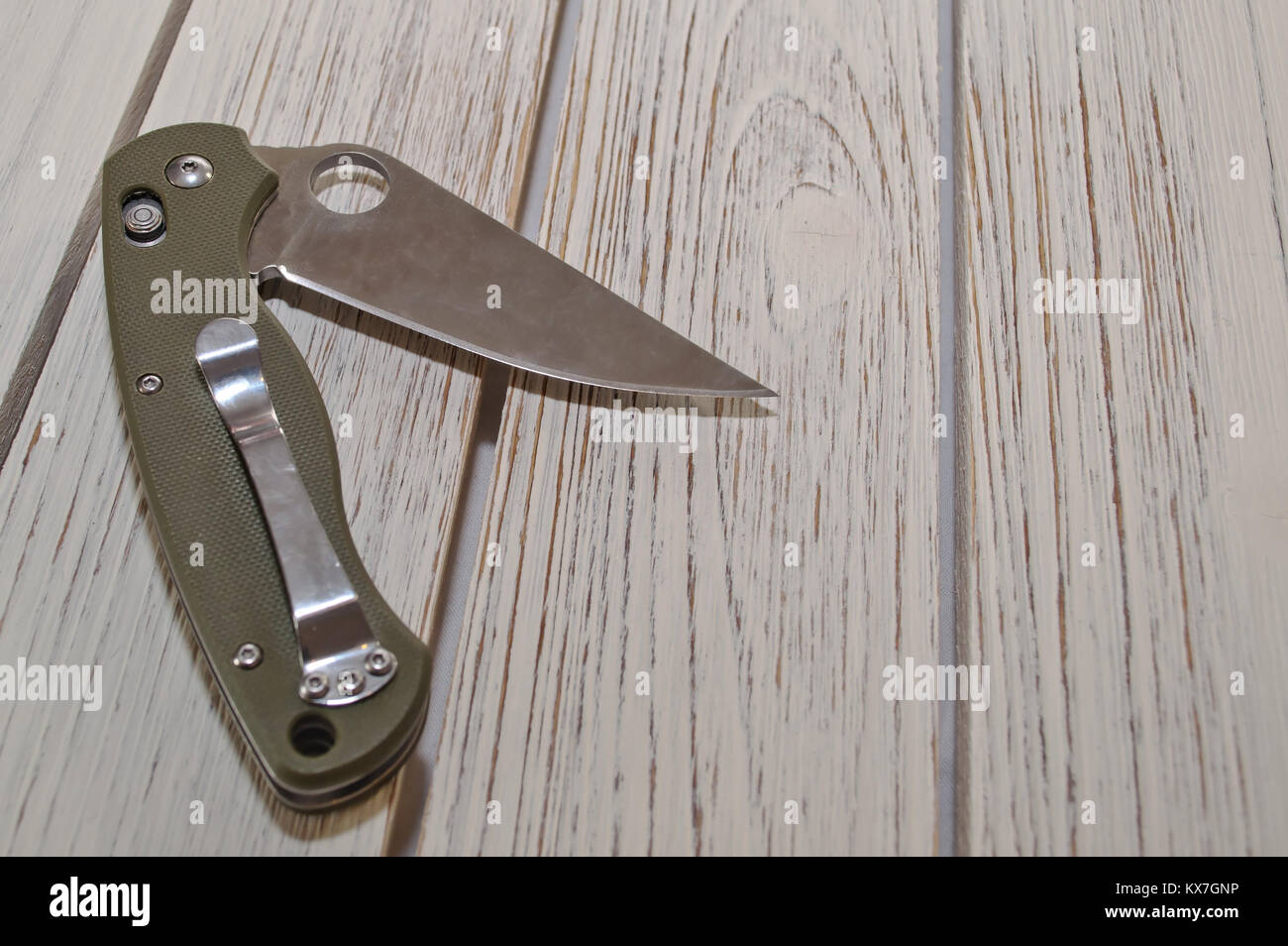 Un aperto coltello tascabile pieghevole con un manico verde posa su un bianco tavolo in legno Foto Stock