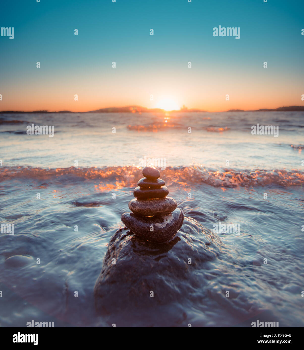 Round pietre lisce in forma piramidale dal mare con onde in arrivo durante il tramonto dorato Foto Stock