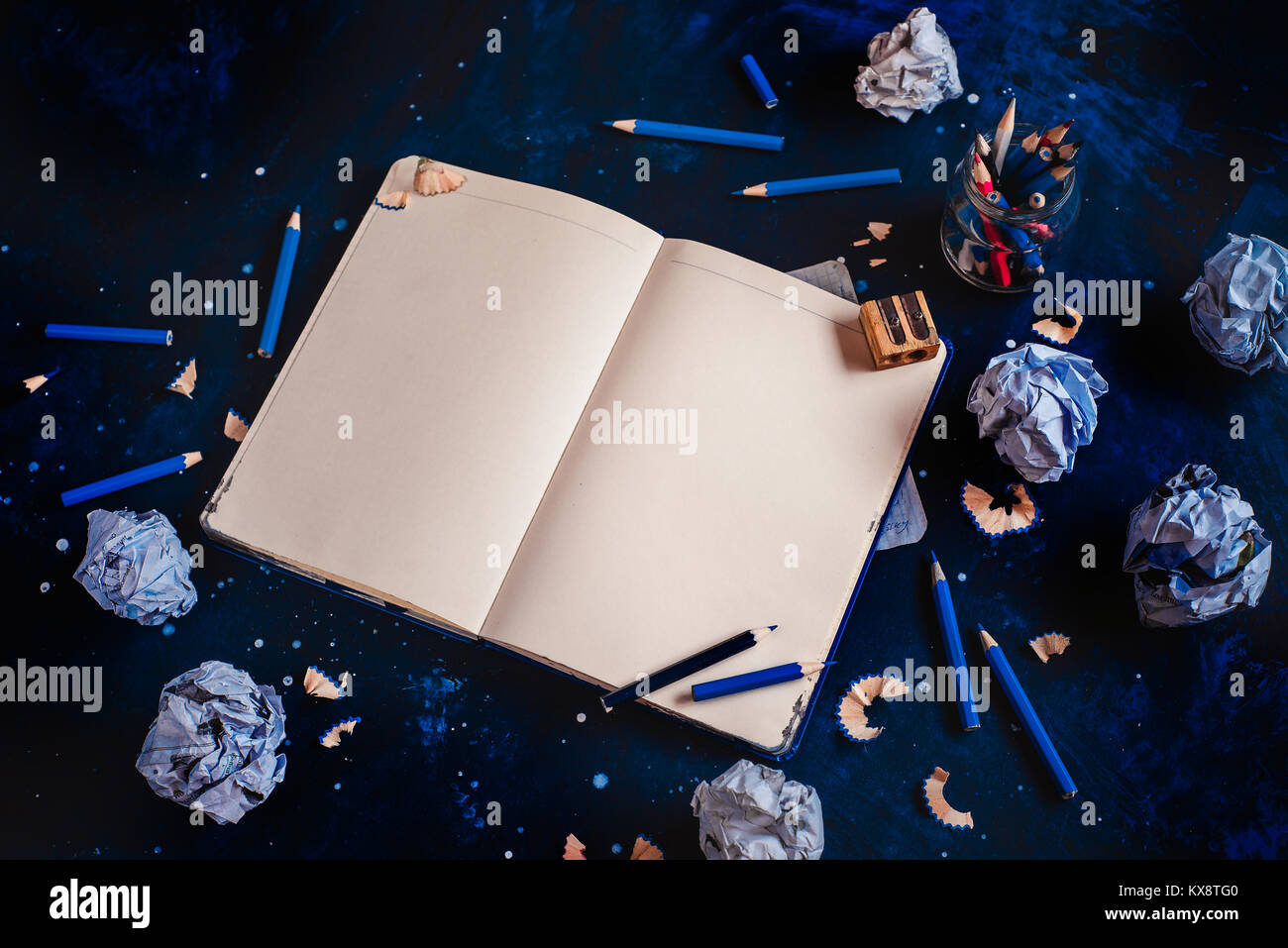 Aprire il blocco note con pagine vuote, carta sgualcita sfere, matite, taccuini e vuoto tazze da caffè su uno sfondo scuro. Ancora vita con lo scrittore workplace. C Foto Stock