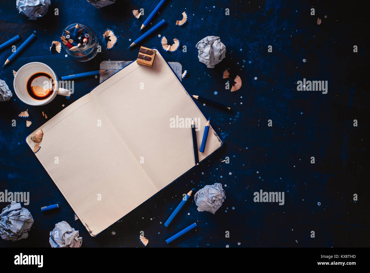 Aprire il blocco note con pagine vuote, carta sgualcita sfere, matite, taccuini e vuoto tazze da caffè su uno sfondo scuro. Ancora vita con lo scrittore workplace. C Foto Stock