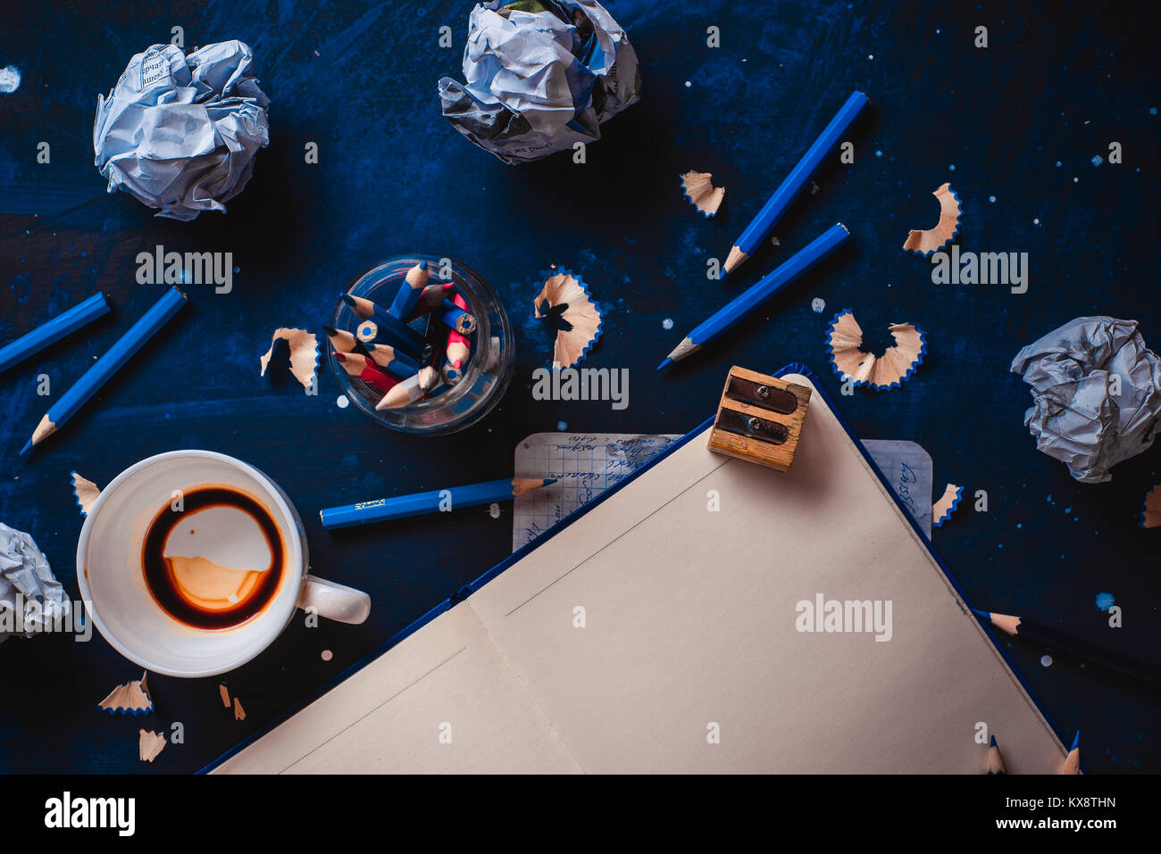 Aprire il blocco note con pagine vuote, carta sgualcita sfere, matite, taccuini e vuoto tazze da caffè su uno sfondo scuro. Ancora vita con lo scrittore workplace. C Foto Stock