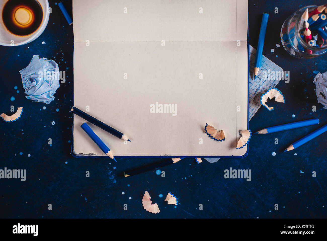 Blocco di scrittori concetto aperto con Blocco note, vuoto tazze da caffè, matite e carta sgualcita palle su uno sfondo scuro. Posto di lavoro creativo. Editing e copywriting concetto. Foto Stock