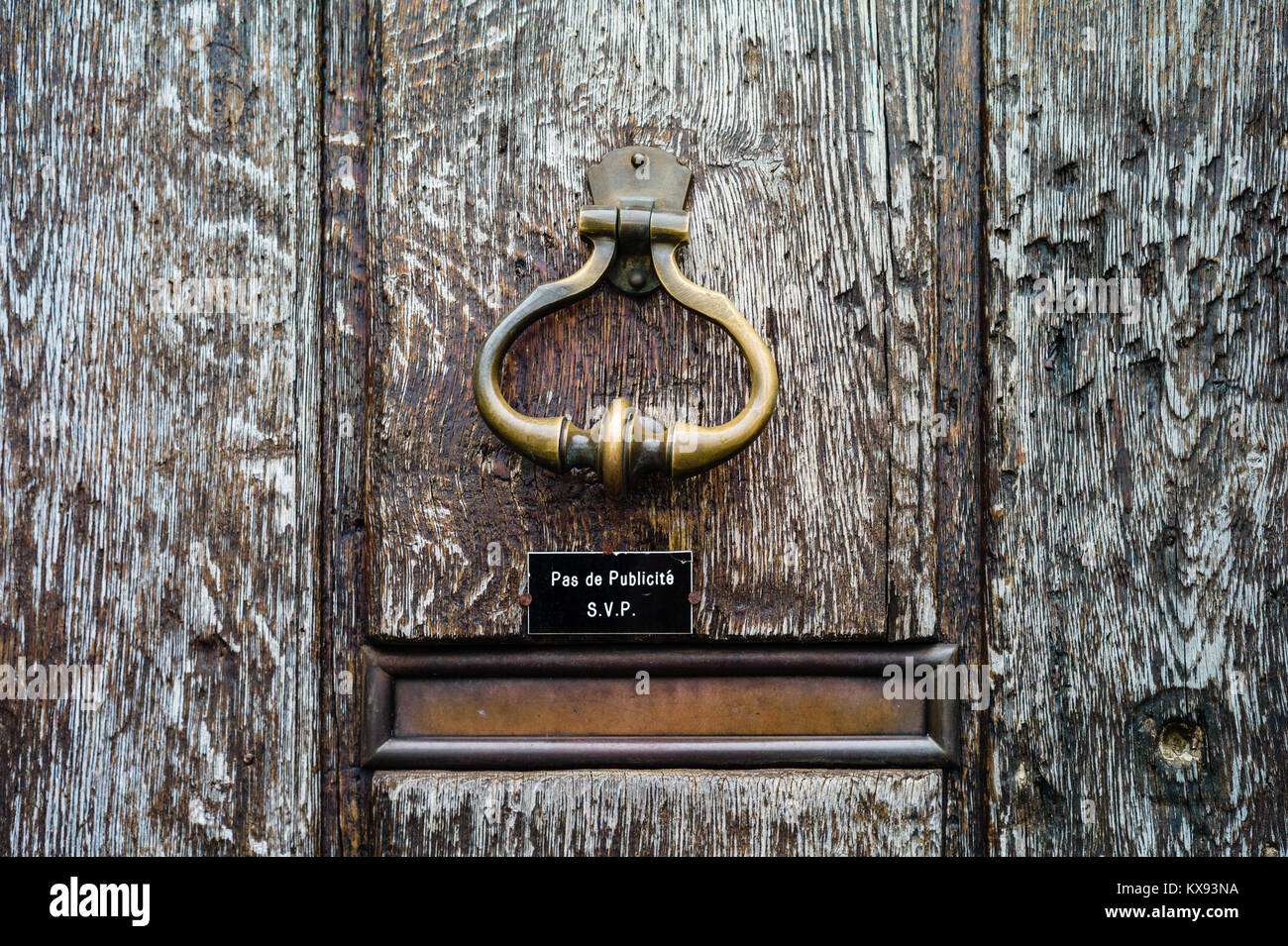 Vista frontale di un ottone vintage respingente della porta e di una cassetta postale dotata di slot su una vecchia porta di legno. Il testo sul segno dice "No la posta indesiderata si prega di'. Foto Stock